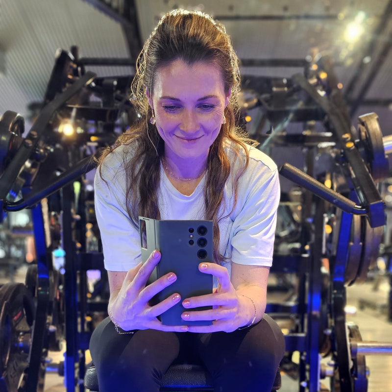 Person taking a mirror selfie in a gym setting with equipment visible