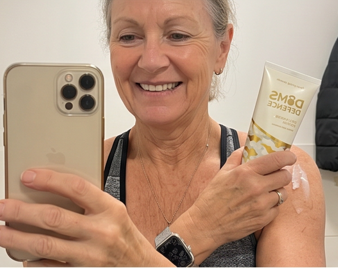 Woman taking a selfie with a phone, holding a tube of DOMS Defense. 