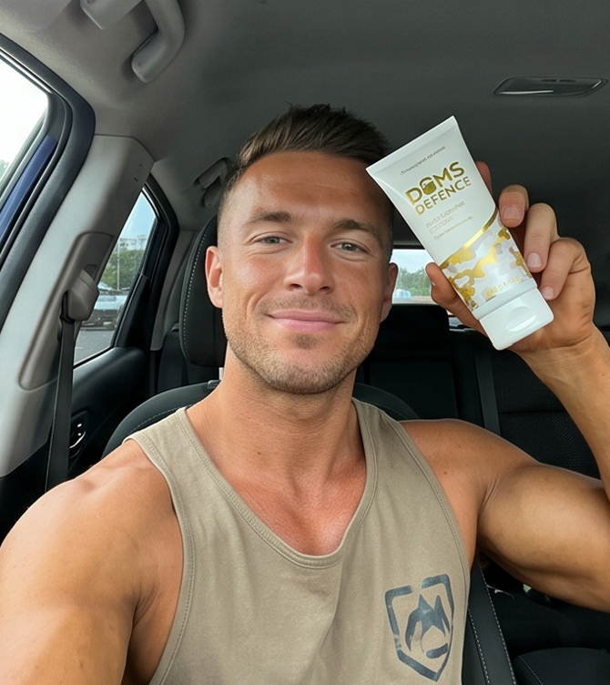 Man sitting in a car holding a sore muscle cream container labeled 'DOMS Defence'.
